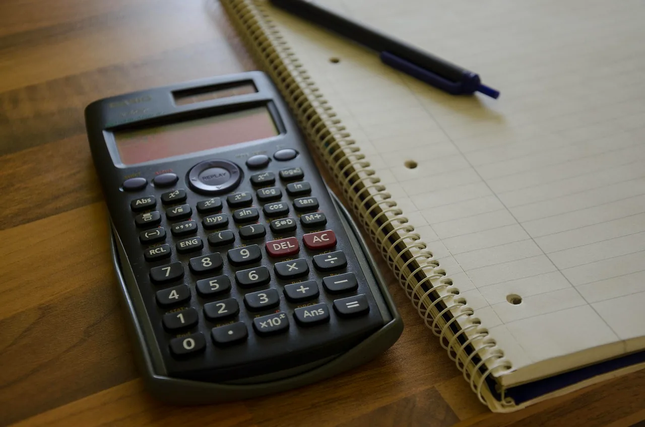 Calculatrice et carnet à spirale posés sur un bureau en bois, préparation d'une demande de documentation